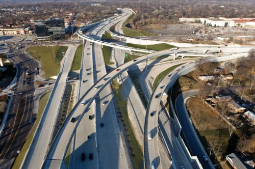 A complex overpass featuring four bridges overlapping each other on Interstate 64. The bridges form an intricate, multi-level structure, with vehicles moving in various directions on the different layers. The crisscrossing roads and support beams create a striking visual of engineering and traffic flow management against the backdrop of the highway.